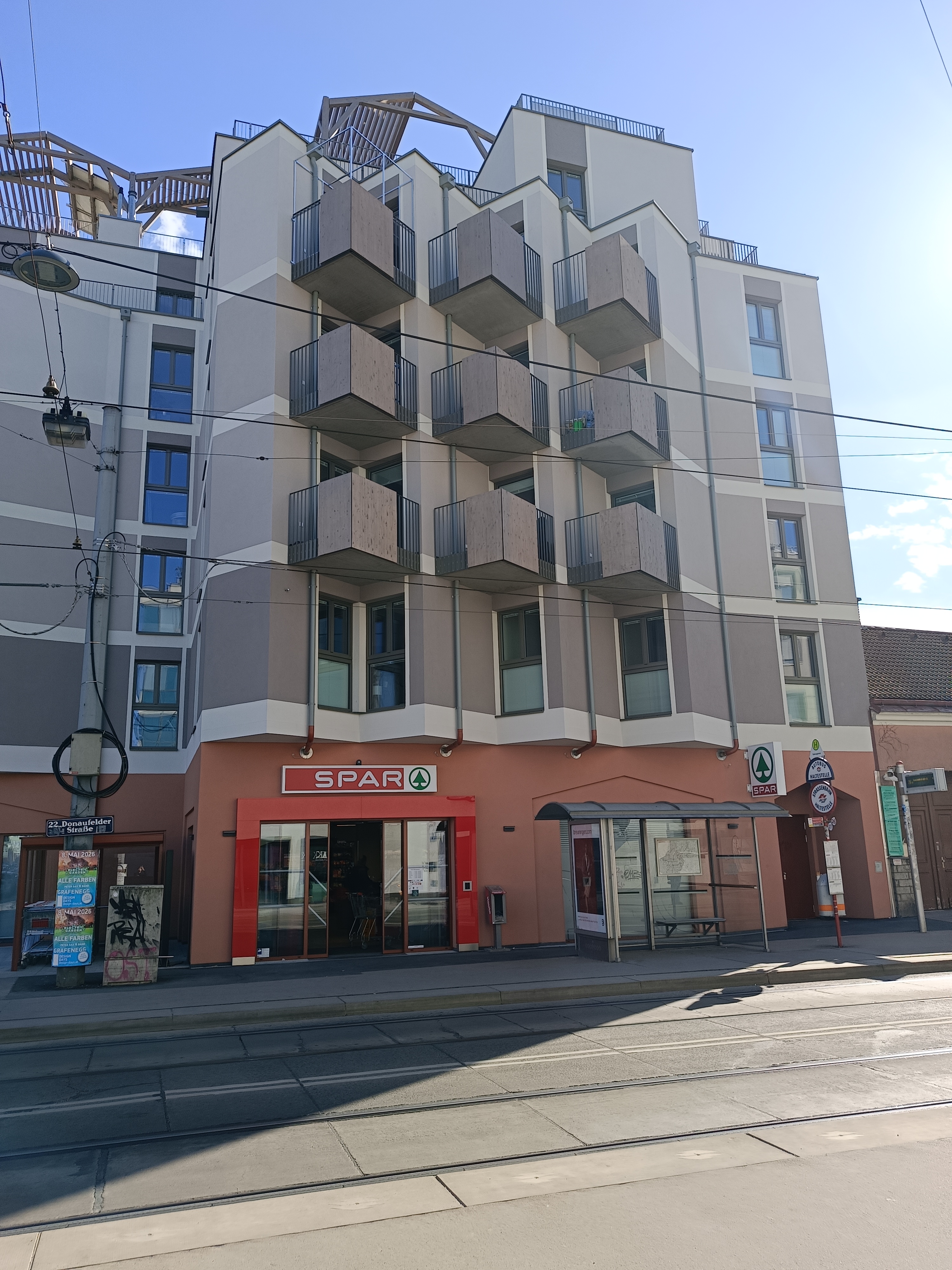 Vorderansicht der "Roten Emma" mit Straßenbahnstation Saikogasse und einem Lebensmittelgeschäft Spar